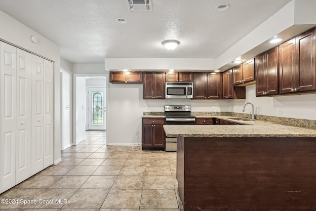 kitchen featuring light stone countertops, sink, stainless steel appliances, kitchen peninsula, and a textured ceiling