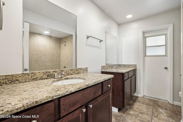 full bathroom with a tile shower, two vanities, baseboards, recessed lighting, and toilet