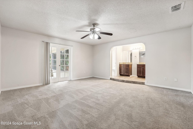 unfurnished living room with ceiling fan, arched walkways, carpet floors, baseboards, and a textured ceiling