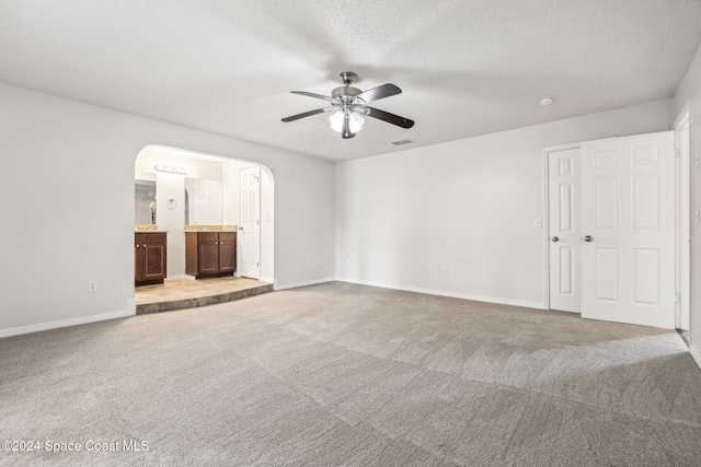 unfurnished living room with ceiling fan, carpet floors, arched walkways, baseboards, and a textured ceiling