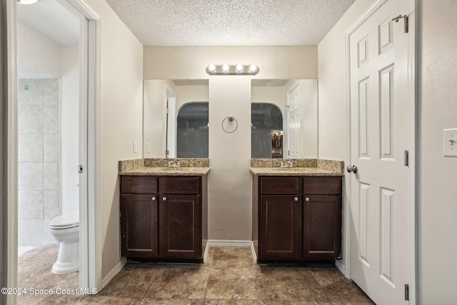 bathroom featuring a textured ceiling, two vanities, toilet, and baseboards