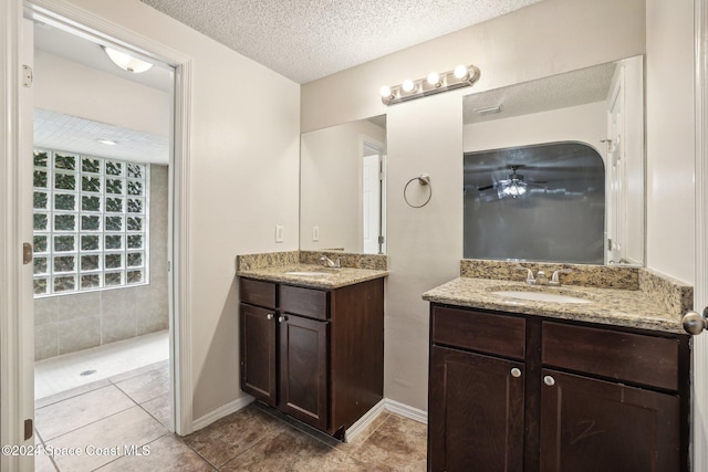 full bathroom with two vanities, a textured ceiling, tiled shower, ceiling fan, and tile patterned floors