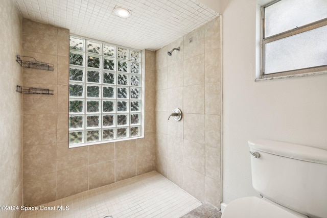 bathroom featuring tile patterned flooring, a healthy amount of sunlight, toilet, and tiled shower