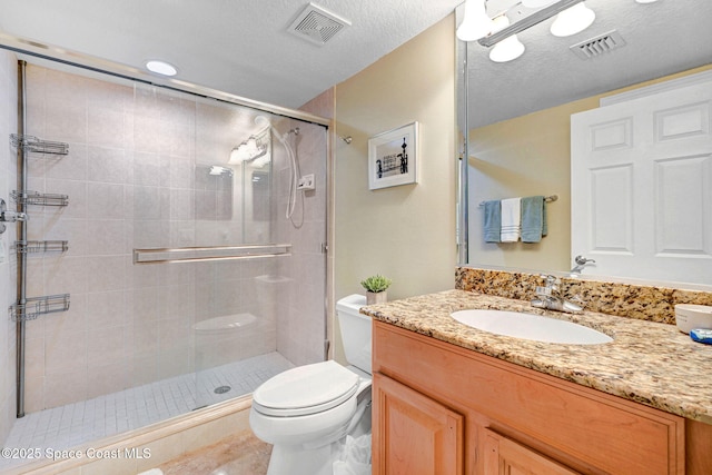 bathroom featuring vanity, toilet, a shower with door, and a textured ceiling