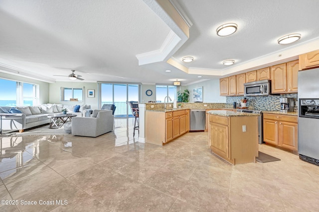 kitchen with light stone countertops, kitchen peninsula, a tray ceiling, appliances with stainless steel finishes, and ornamental molding