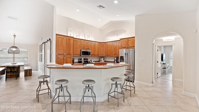 kitchen featuring an island with sink, light tile patterned flooring, a kitchen bar, appliances with stainless steel finishes, and high vaulted ceiling