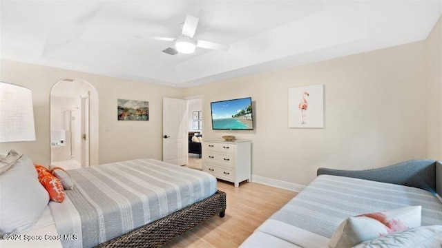 bedroom with ensuite bathroom, a tray ceiling, light hardwood / wood-style floors, and ceiling fan