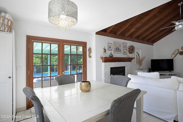 tiled dining area with french doors, a fireplace, ceiling fan with notable chandelier, and vaulted ceiling