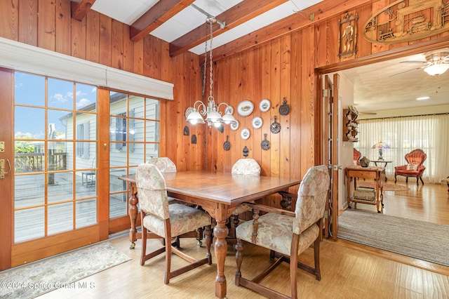 dining room with wood walls, beamed ceiling, an inviting chandelier, and hardwood / wood-style floors