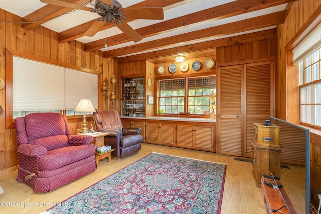 sitting room featuring beam ceiling, wooden walls, light hardwood / wood-style flooring, and ceiling fan