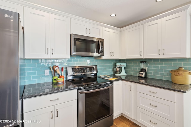 kitchen featuring stainless steel appliances, dark stone counters, white cabinetry, light hardwood / wood-style floors, and tasteful backsplash