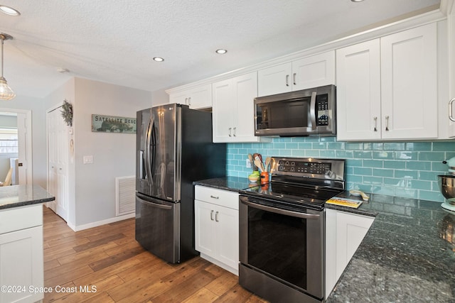 kitchen with backsplash, decorative light fixtures, white cabinetry, light wood-type flooring, and appliances with stainless steel finishes