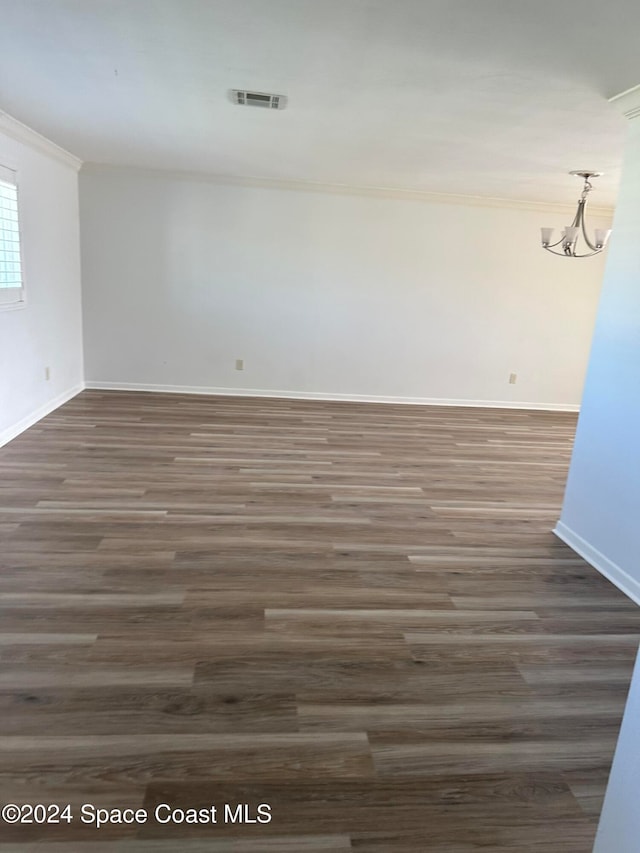 empty room featuring crown molding, a notable chandelier, and dark hardwood / wood-style flooring