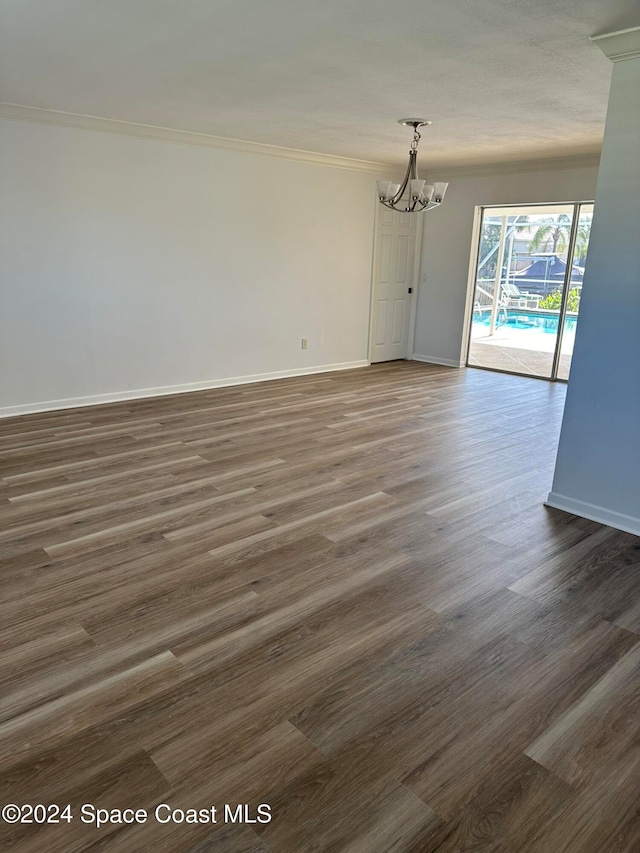 spare room featuring ornamental molding, dark wood-type flooring, and a notable chandelier