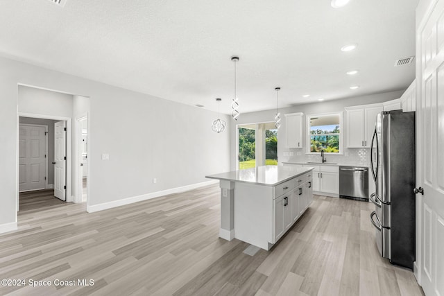 kitchen with white cabinets, decorative light fixtures, a kitchen island, and appliances with stainless steel finishes