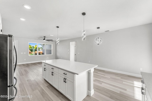 kitchen with white cabinets, light wood-type flooring, decorative light fixtures, and stainless steel refrigerator