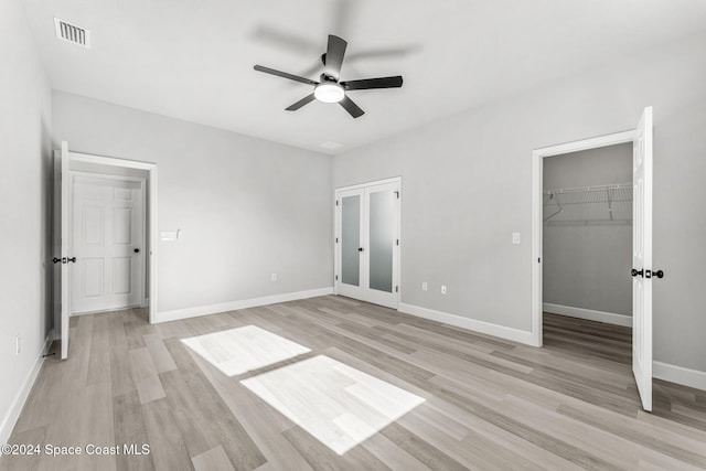 unfurnished bedroom featuring ceiling fan, light hardwood / wood-style floors, a spacious closet, and french doors