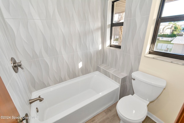 bathroom with tile walls, hardwood / wood-style floors, a bathtub, and toilet