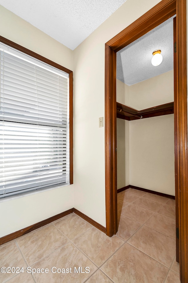 hall with a textured ceiling and light tile patterned floors