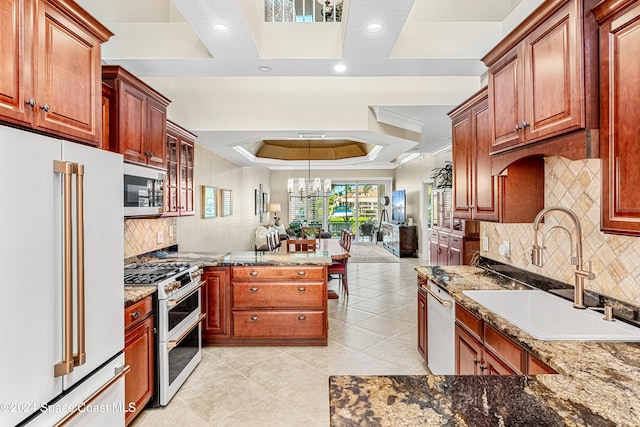 kitchen featuring high quality appliances, dark stone countertops, sink, an inviting chandelier, and a raised ceiling