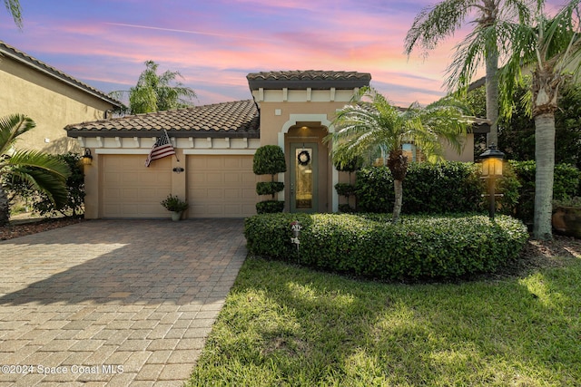 mediterranean / spanish-style home with a garage, stucco siding, decorative driveway, and a tile roof