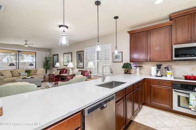 kitchen with hanging light fixtures, a sink, stainless steel appliances, open floor plan, and backsplash
