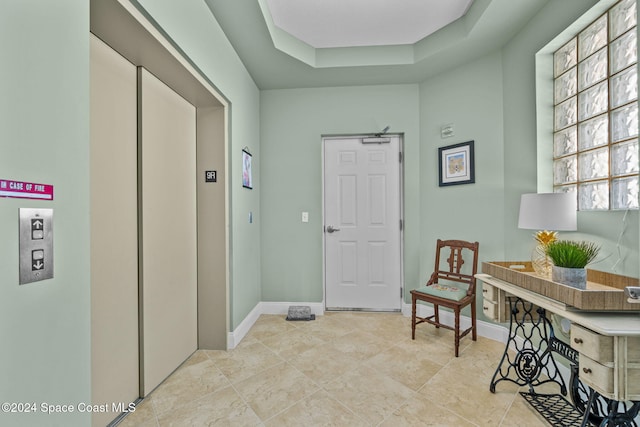 hallway featuring elevator, light tile patterned floors, and a raised ceiling