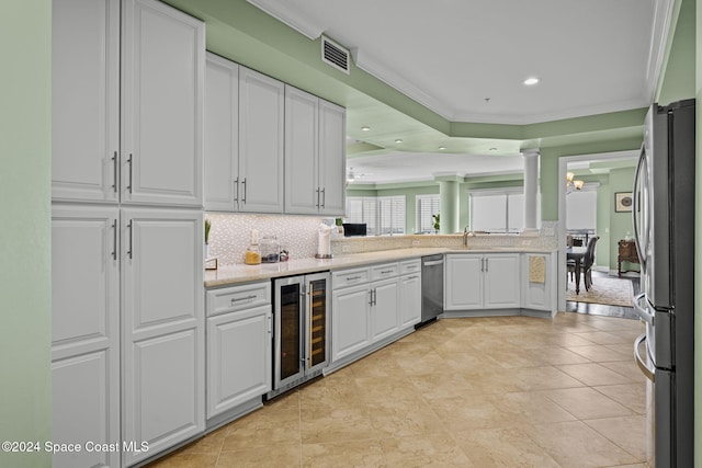 kitchen with wine cooler, ornamental molding, decorative columns, white cabinets, and stainless steel refrigerator