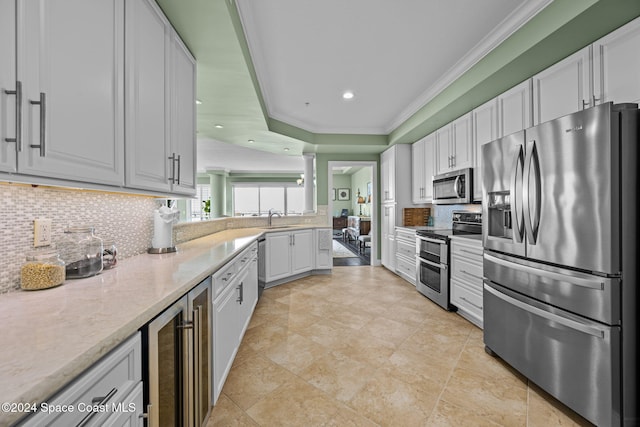 kitchen with appliances with stainless steel finishes, sink, white cabinets, wine cooler, and ornamental molding