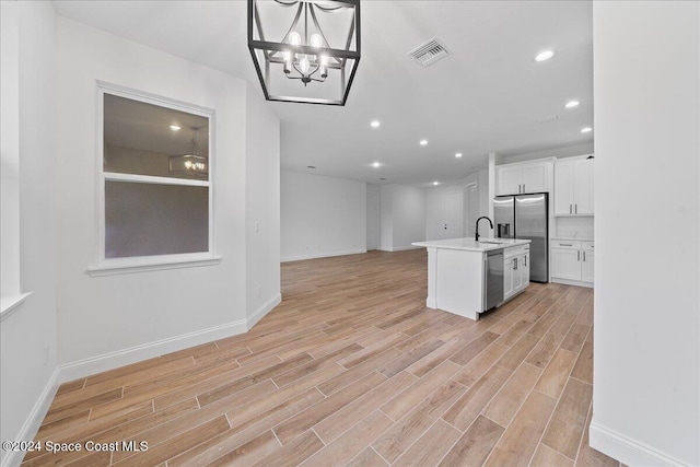 kitchen with appliances with stainless steel finishes, a kitchen island with sink, sink, light hardwood / wood-style flooring, and white cabinets