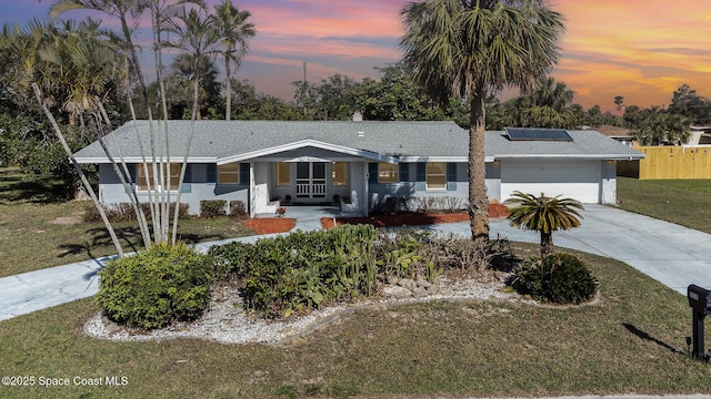 single story home with a lawn, a garage, and solar panels