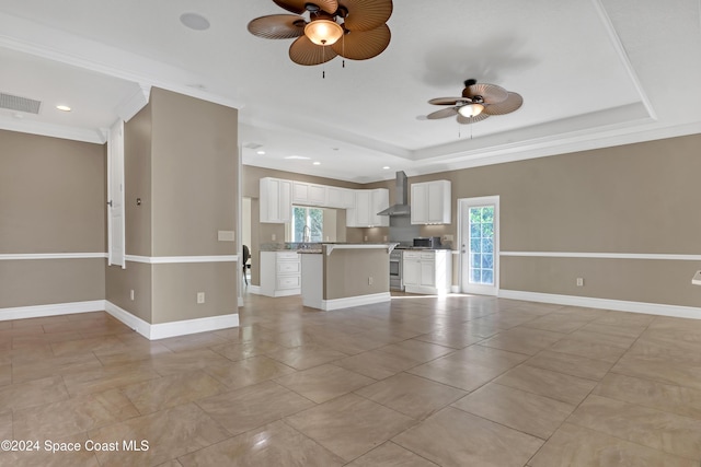 unfurnished living room with a wealth of natural light, visible vents, a raised ceiling, and a ceiling fan