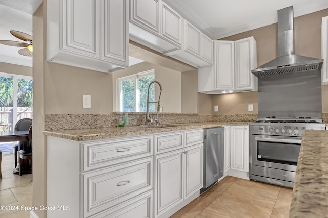 kitchen with light tile patterned floors, wall chimney exhaust hood, a ceiling fan, appliances with stainless steel finishes, and plenty of natural light