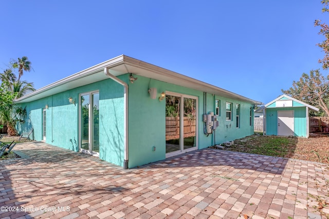 rear view of house featuring a patio, an outbuilding, a storage unit, stucco siding, and fence