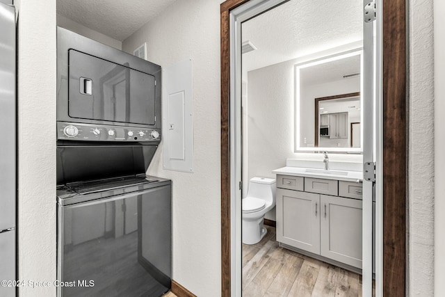 bathroom with stacked washing machine and dryer, wood finished floors, a textured ceiling, vanity, and toilet