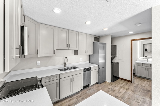 kitchen with stacked washer and clothes dryer, stainless steel appliances, a sink, gray cabinets, and a textured ceiling