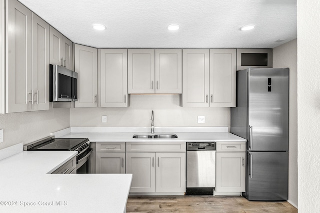 kitchen featuring appliances with stainless steel finishes, a sink, gray cabinets, light countertops, and light wood-style flooring
