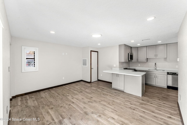 kitchen featuring stainless steel appliances, a sink, gray cabinets, a peninsula, and light countertops