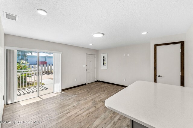 unfurnished dining area with a textured ceiling, light wood-style flooring, recessed lighting, and baseboards