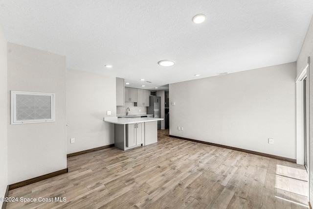 kitchen featuring light countertops, freestanding refrigerator, a peninsula, light wood-type flooring, and a textured ceiling