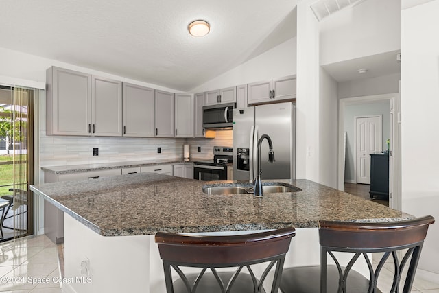 kitchen with lofted ceiling, a center island with sink, a breakfast bar area, dark stone countertops, and stainless steel appliances