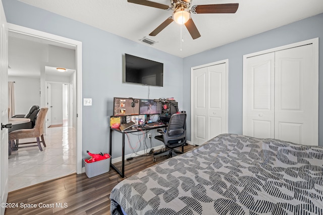 bedroom featuring two closets, hardwood / wood-style flooring, and ceiling fan