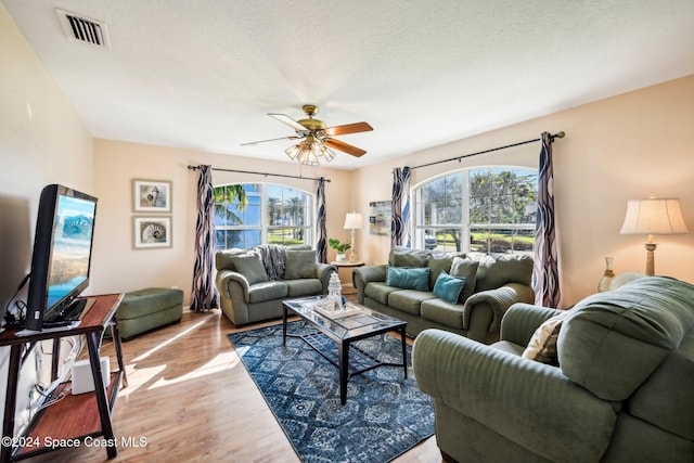 living room with light hardwood / wood-style floors, a textured ceiling, and ceiling fan