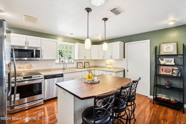 kitchen featuring sink, a kitchen island, stainless steel appliances, white cabinets, and dark wood-type flooring