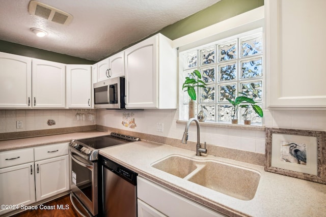 kitchen featuring stainless steel appliances, sink, white cabinetry, a textured ceiling, and tasteful backsplash