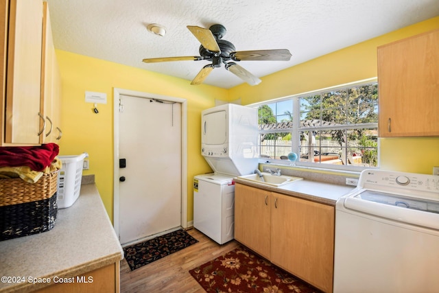 laundry room with sink, light wood-type flooring, a textured ceiling, stacked washing maching and dryer, and cabinets