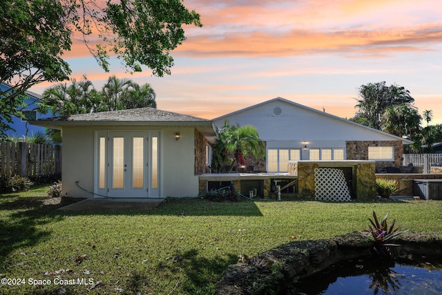 back house at dusk featuring french doors and a yard