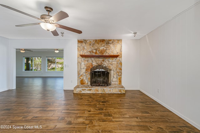 unfurnished living room featuring dark wood-type flooring, ceiling fan, and a stone fireplace