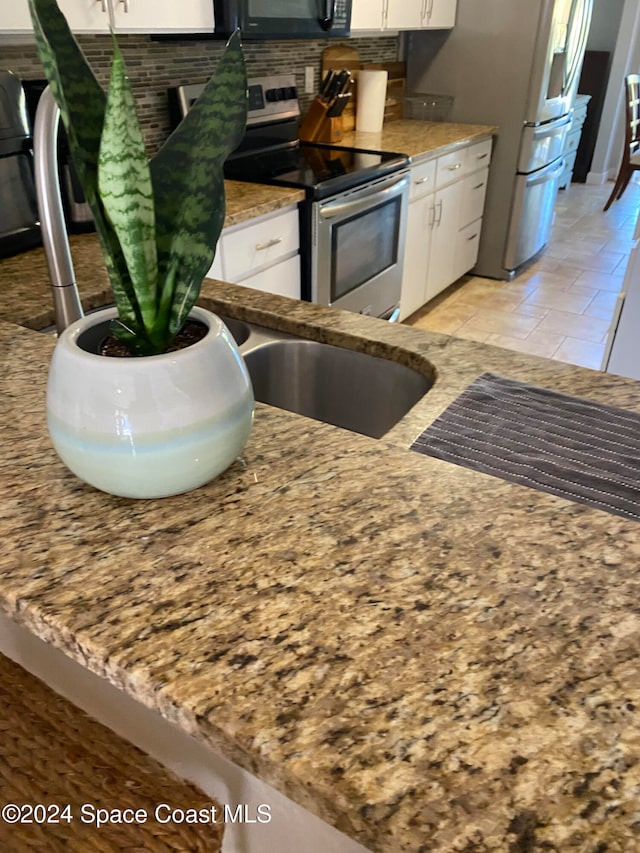 kitchen featuring light stone countertops, decorative backsplash, white cabinets, and stainless steel appliances