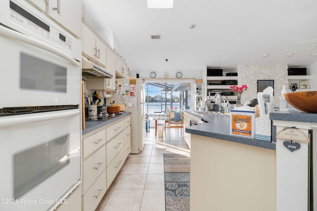 kitchen featuring a large fireplace, light tile patterned floors, cream cabinetry, sink, and white appliances